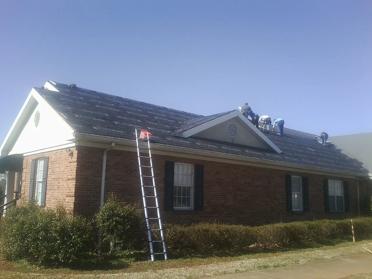 Crew tearing shingles off a brick ranch roof with a ladder set — Metal Roof Repair work by our crew in Universal City