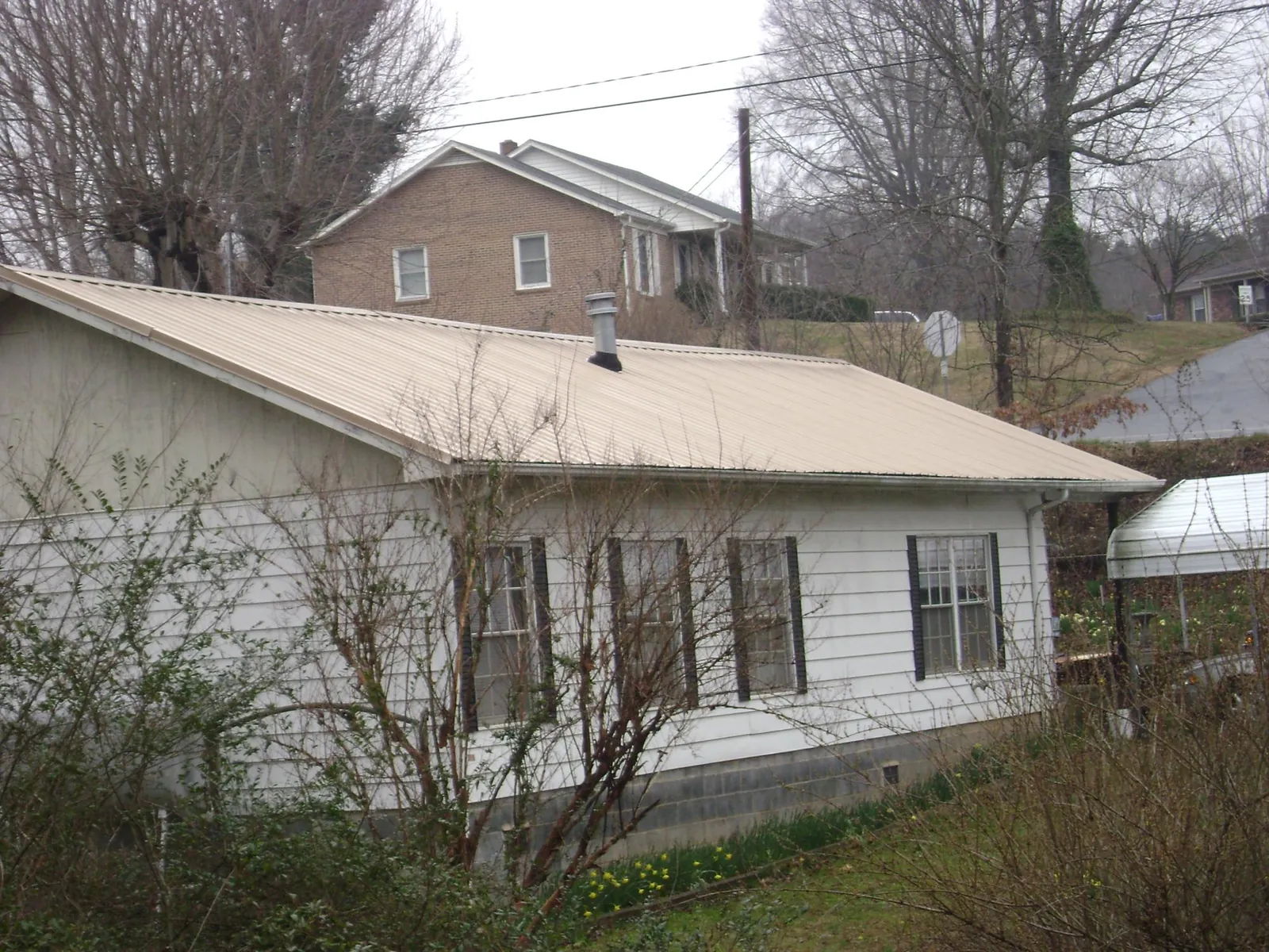 Tan metal roof on a white sided house set into a hillside — Commercial Roofing by Roofing Brothers in Universal City